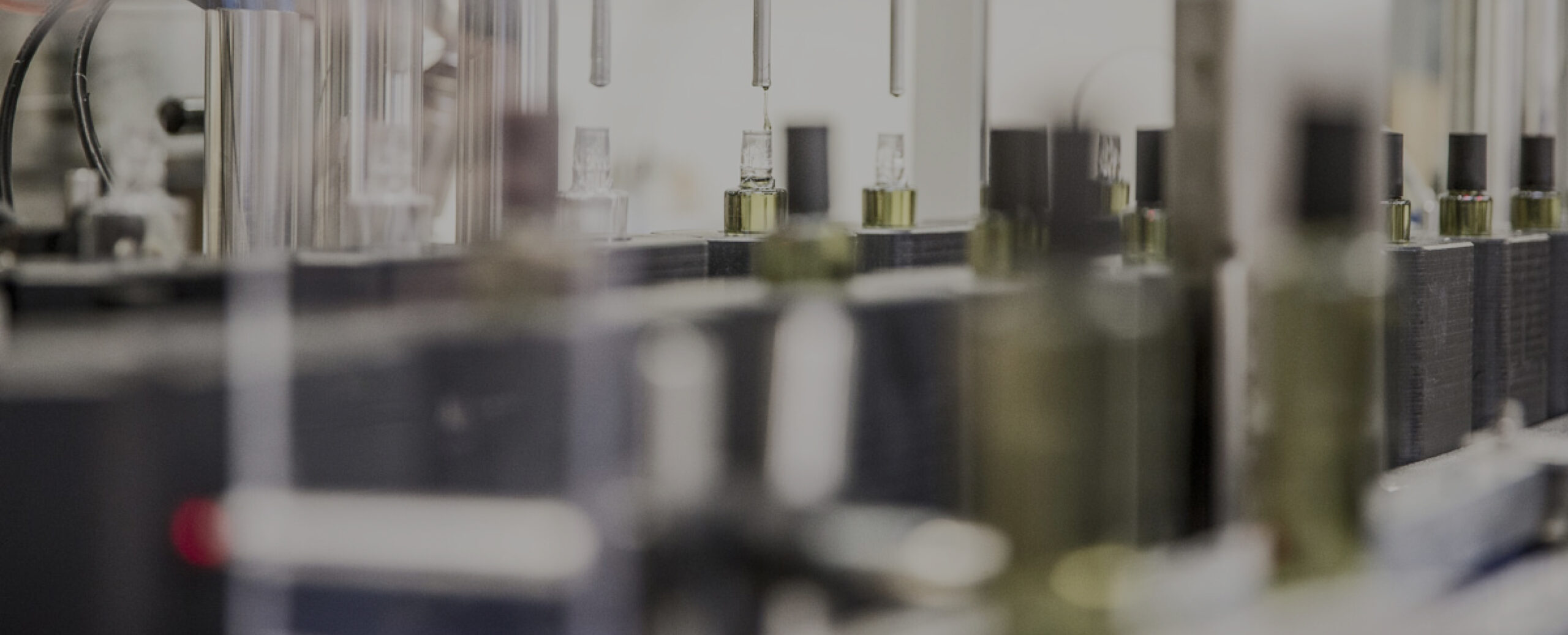 Um fundo desfocado de equipamento de laboratório com tubos e recipientes de vidro, indicando um ambiente científico ou industrial.