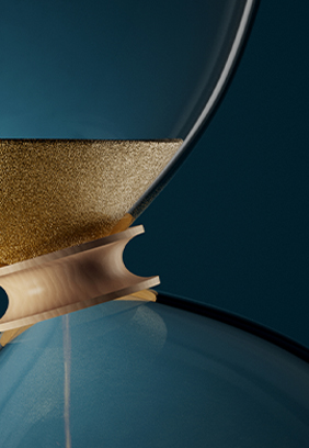 Nahaufnahme einer dekorativen Sanduhr mit einer goldenen und hölzernen Klammer, die zwei Glaskolben verbindet, vor einem dunkelblauen Hintergrund.