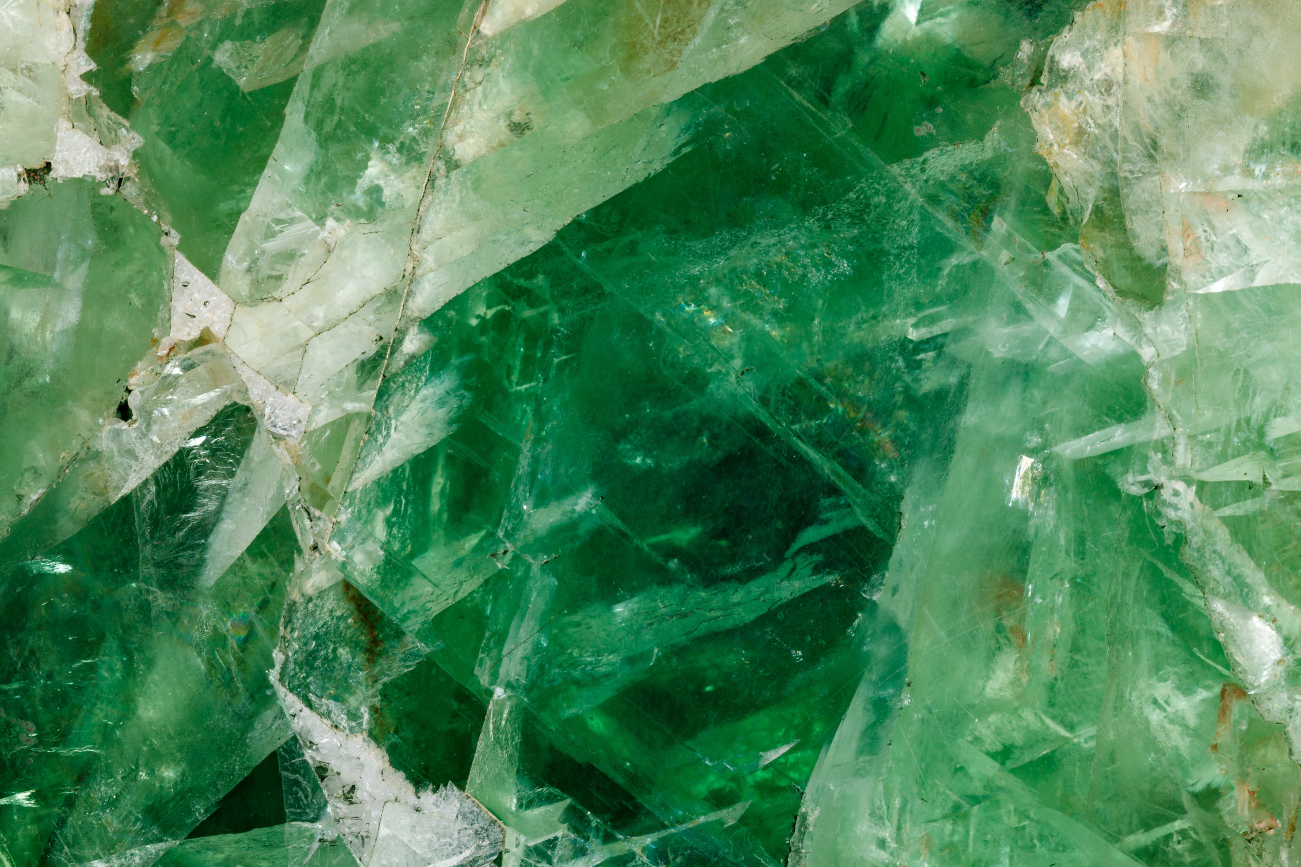 Nahaufnahme eines kristallinen grünen Minerals mit unterschiedlichen Grüntönen und transparenten Abschnitten. Die Textur wirkt kantig und facettiert und zeichnet sich durch eine natürliche, schimmernde Qualität aus.