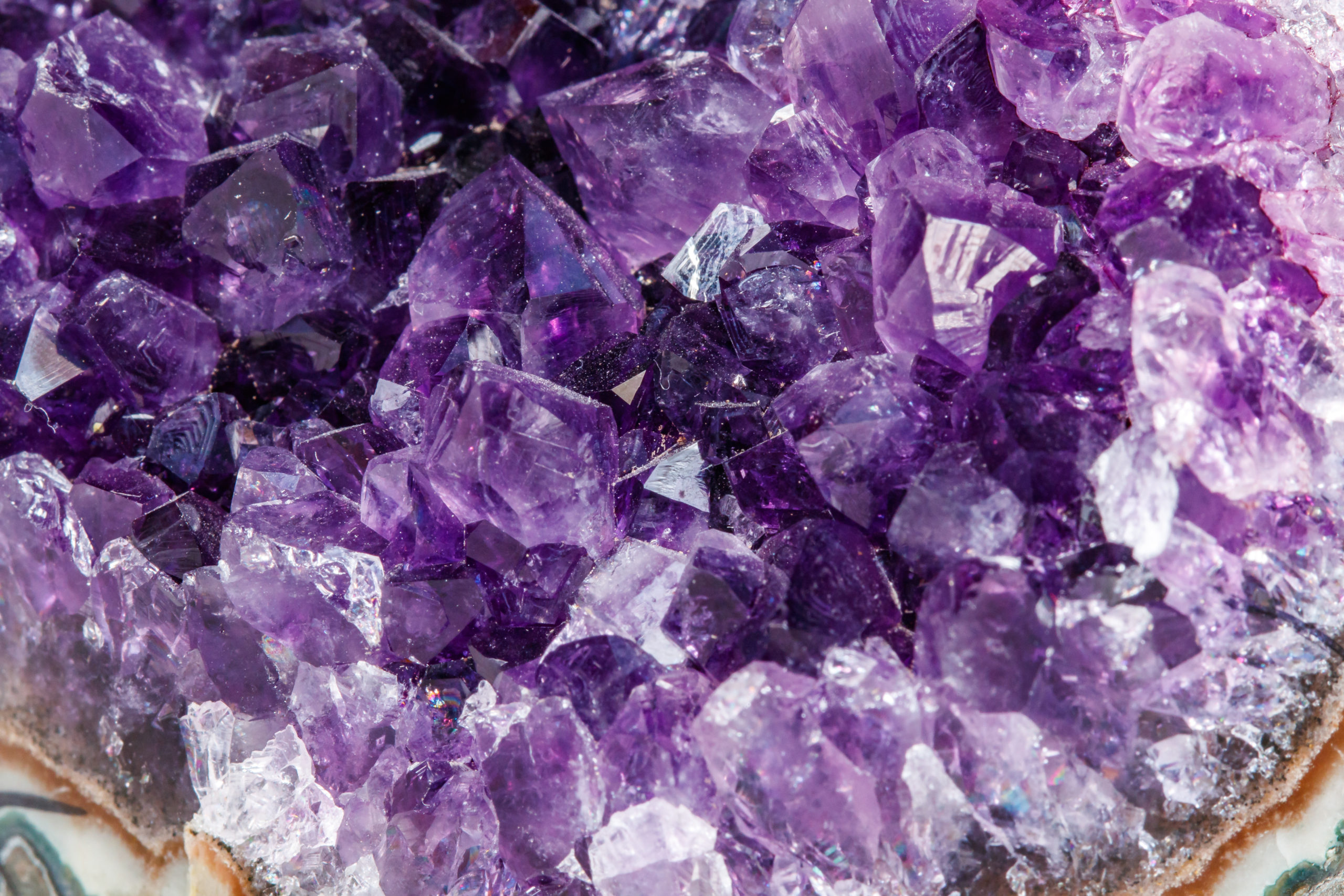 Nahaufnahme einer Gruppe von Amethystkristallen, die verschiedene Violetttöne und eine glänzende, reflektierende Oberfläche aufweisen.