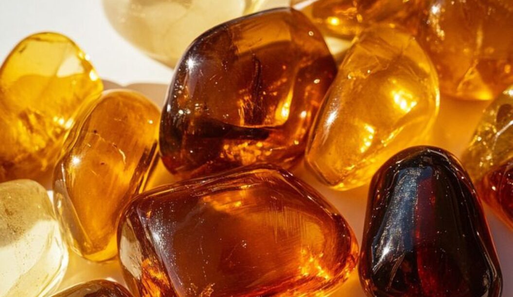 Una varietà di pietre di ambra levigate in diverse tonalità di giallo e marrone, sparse su una superficie chiara.