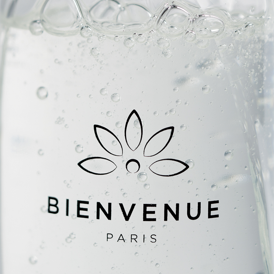 Nahaufnahme einer Flasche Sprudelwasser mit dem Etikett „BIENVENUE PARIS“ und sichtbaren Bläschen in der Flüssigkeit.