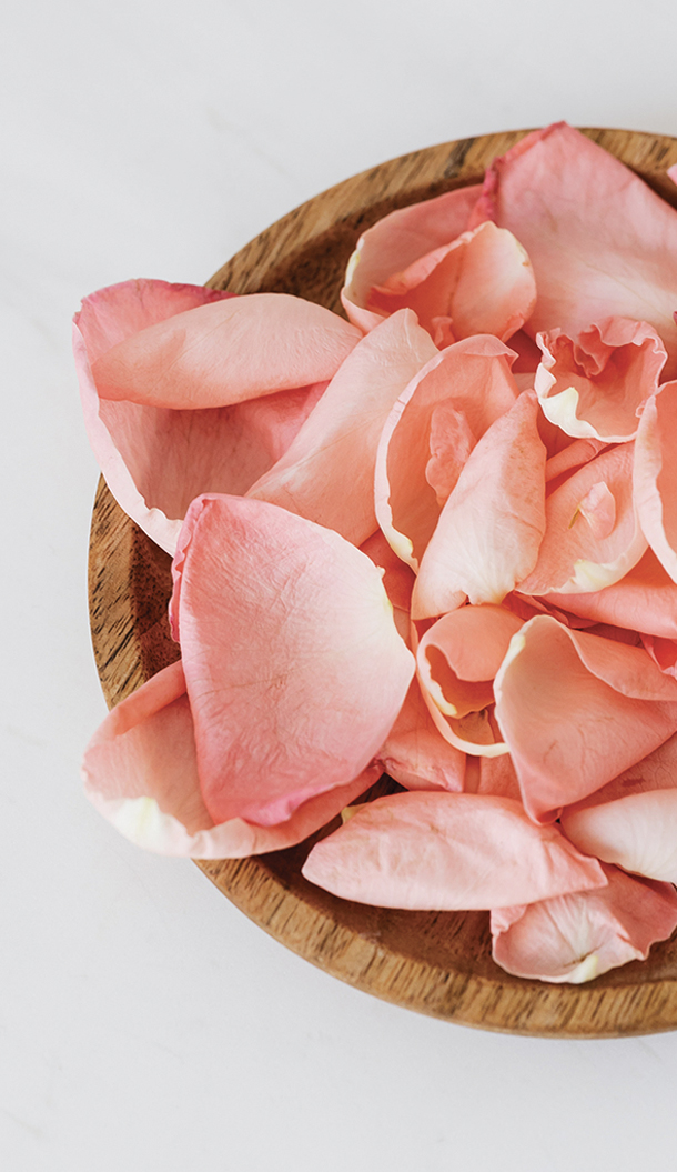 Eine Holzschale, gefüllt mit weichen, rosa Rosenblättern, die ordentlich angeordnet sind.