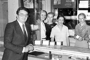 Eine Gruppe von fünf Personen, darunter ein Mann im Anzug und vier Frauen in Businesskleidung, steht hinter einem Tresen, auf dem verschiedene Produkte in einer Ladenumgebung präsentiert werden. Die Umgebung scheint ein Kosmetik- oder Schönheitssalon zu sein.