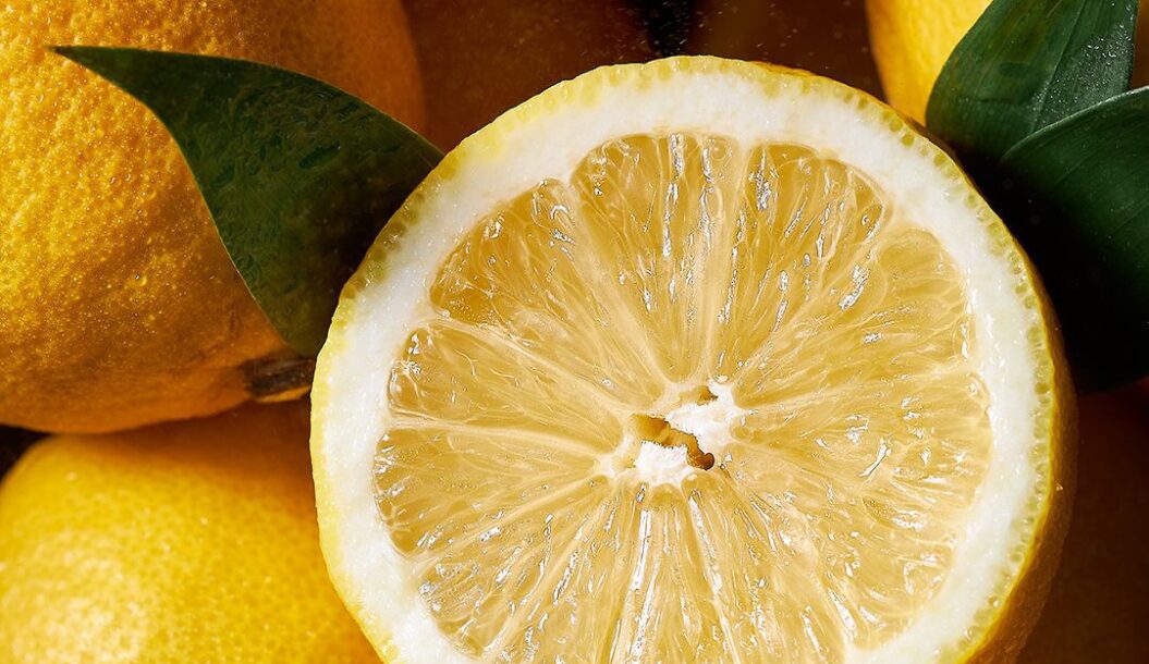 Primo piano di un limone tagliato a metà, che mostra la sua polpa succosa e ricca di texture, circondato da limoni interi e foglie verdi.