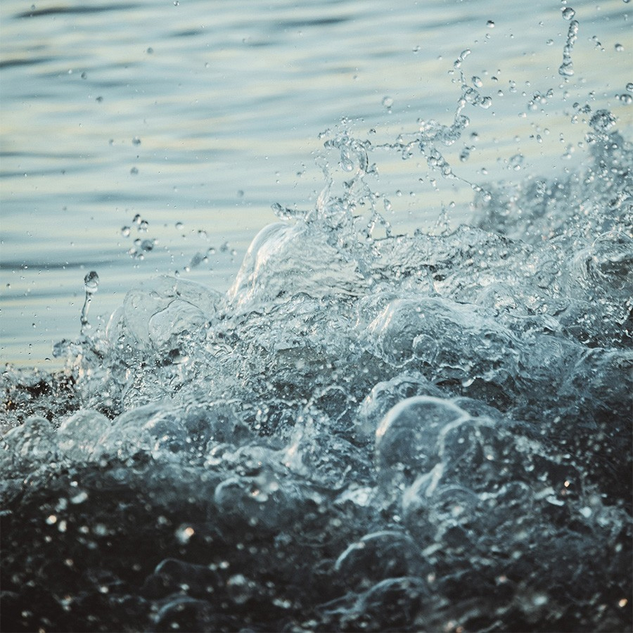 Primo piano di schizzi d'acqua che formano delle bolle, con una superficie calma e riflettente sullo sfondo.