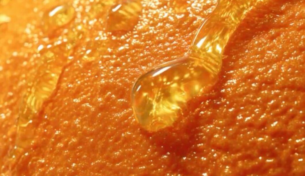 Immagine ravvicinata della superficie ruvida di un'arancia, con goccioline di succo che brillano su di essa.