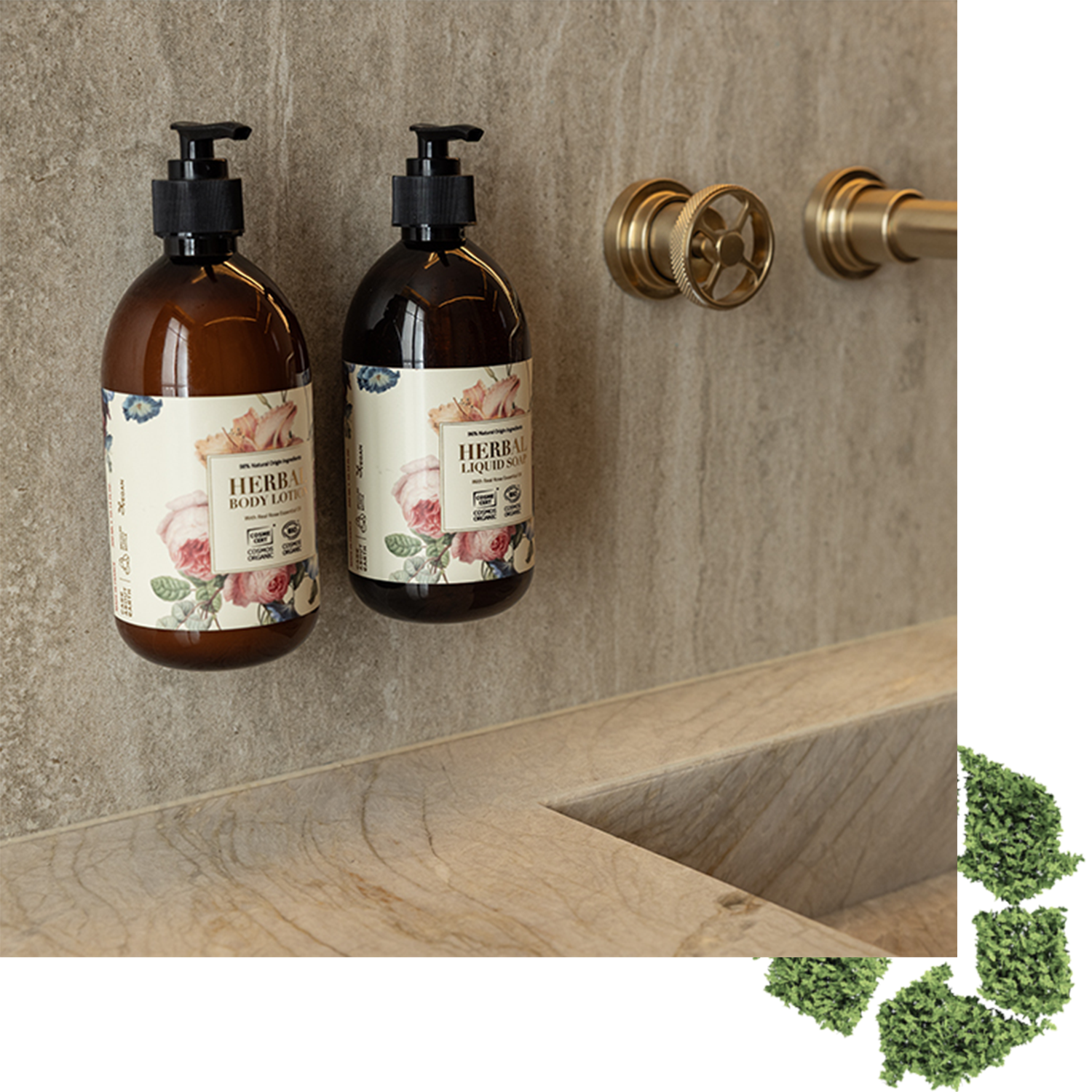 Dois frascos marrons com loção corporal e loção facial à base de ervas estão colocados numa parede de pedra texturizada perto de uma torneira elegante, com um lavatório de pedra sofisticado abaixo e algumas ervas verdes no canto.