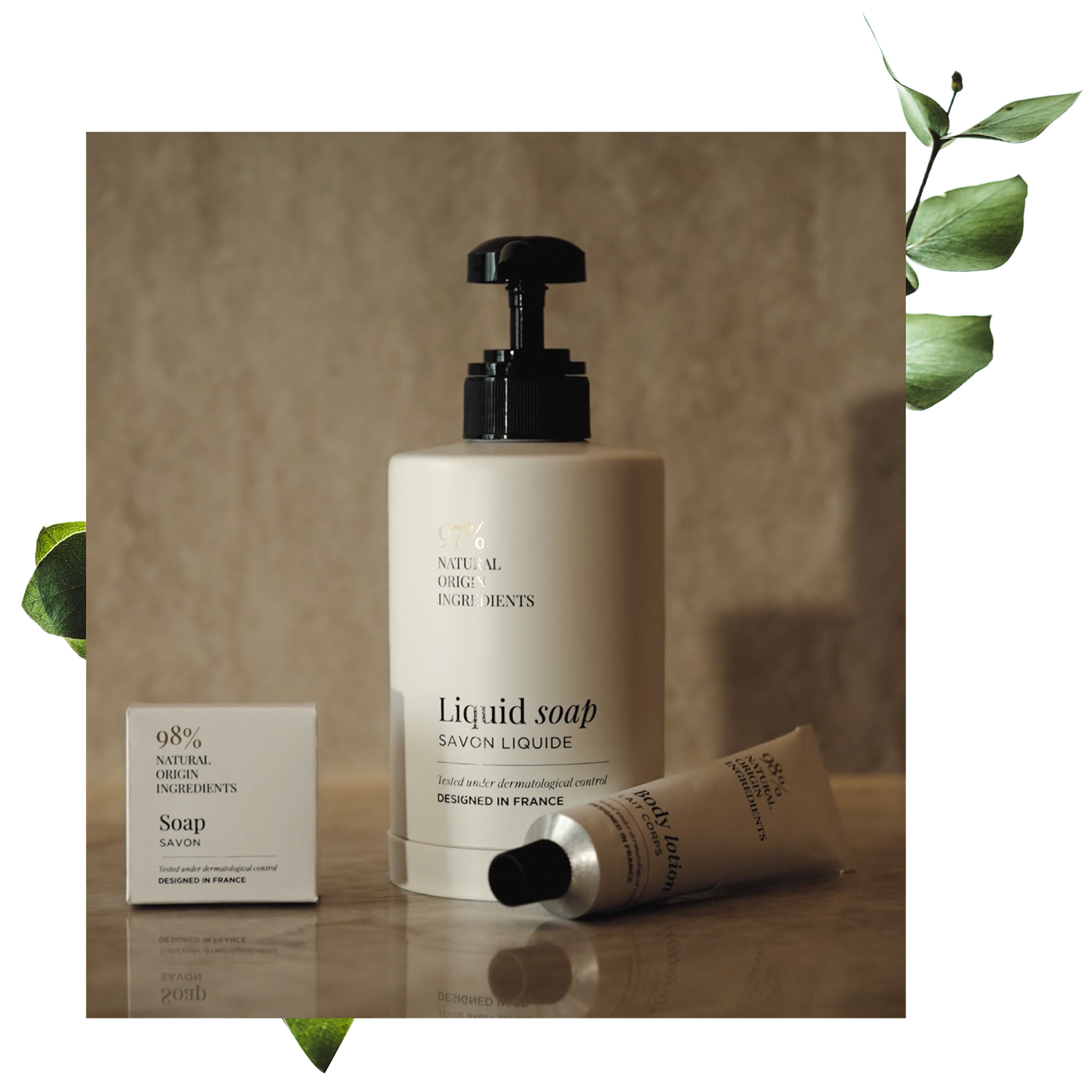 Eine Flasche Flüssigseife mit Pumpspender, dazu ein kleines rechteckiges Stück Seife und eine Tube Creme, alles vor einem strukturierten neutralen Hintergrund mit grünen Blättern.