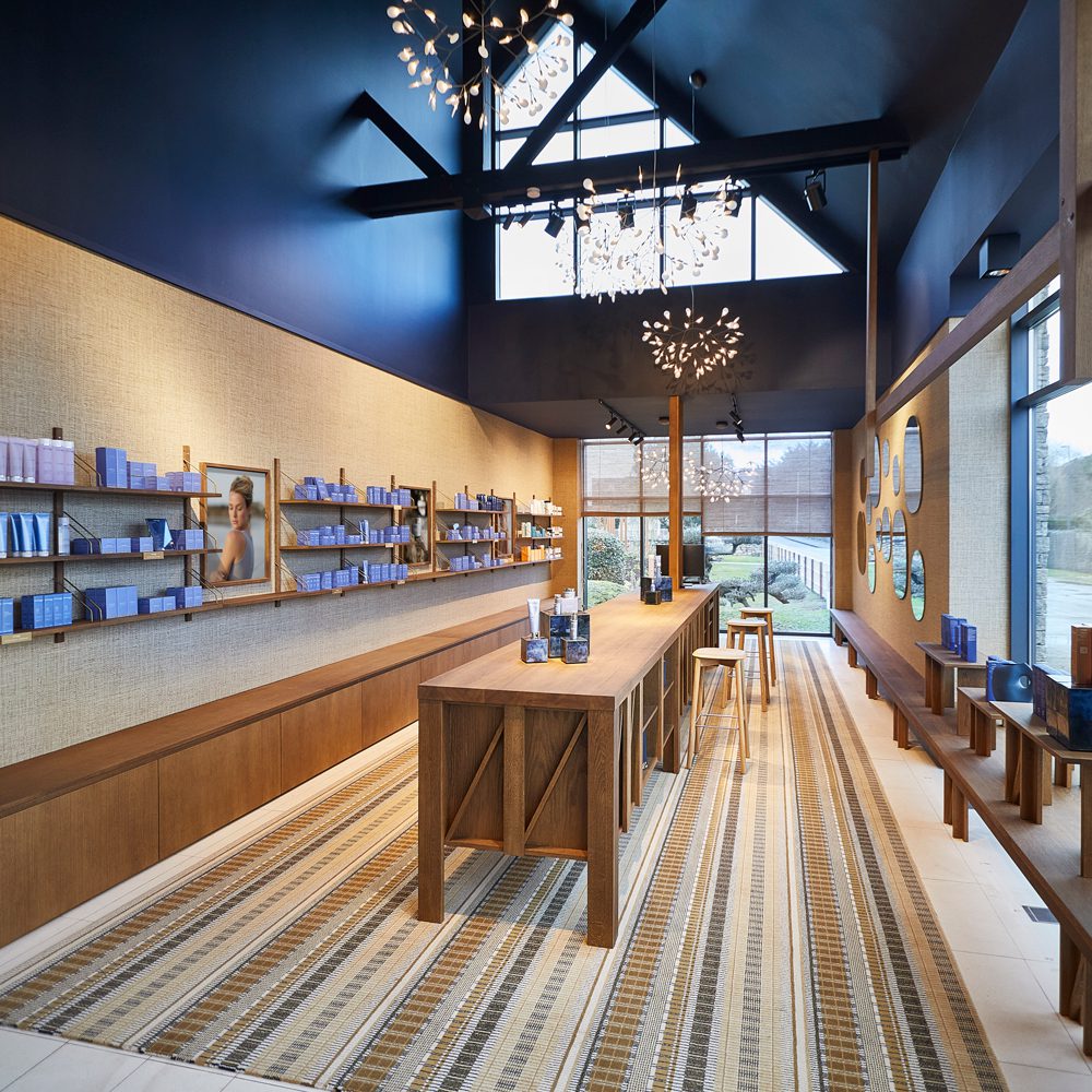 Een moderne winkelruimte met een houten toonbank, schappen met blauwe producten en grote ramen die natuurlijk licht binnenlaten. Het interieur is voorzien van moderne verlichting en een gestructureerde muur.