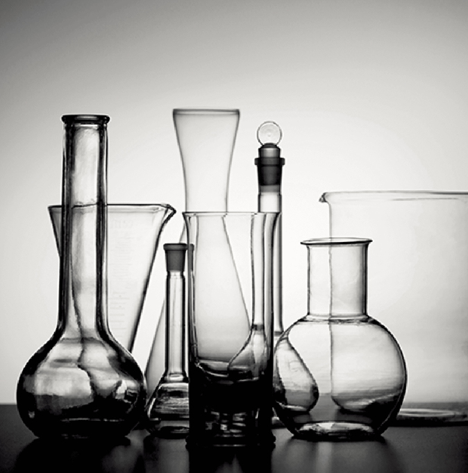 一組各式各樣的玻璃實驗室燒瓶與量筒,以漸變背景為襯,經藝術手法精心排列。這些玻璃器皿形狀與尺寸各異,在單色調光線中折射出瑩瑩光澤。