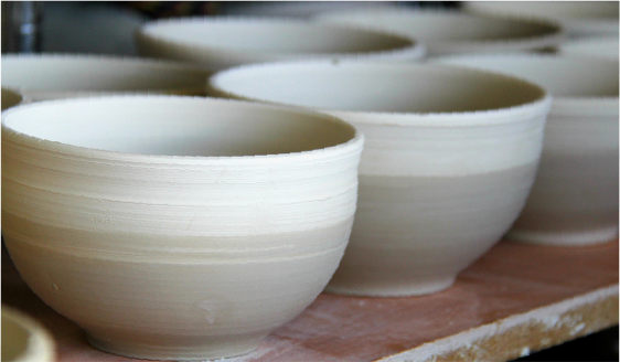 Una collezione di ciotole in ceramica non smaltata disposte in fila, che mettono in risalto le loro superfici lisce e naturali color beige.