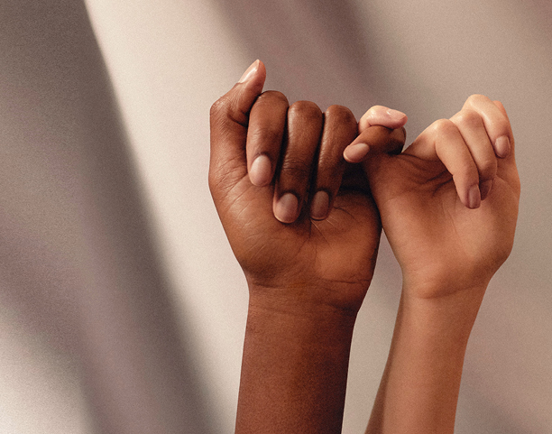 Due mani, una con la pelle più scura e l'altra con la pelle più chiara, sono unite in un gesto di promessa contro uno sfondo delicatamente illuminato.