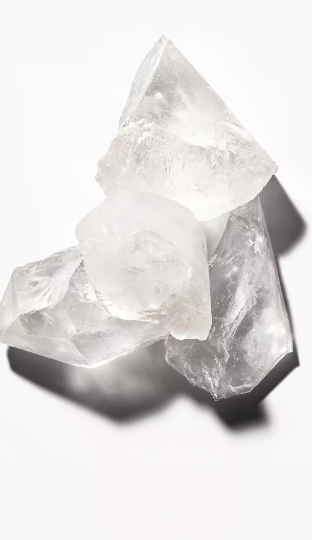 A cluster of clear ice crystals stacked on a white surface, casting subtle shadows.