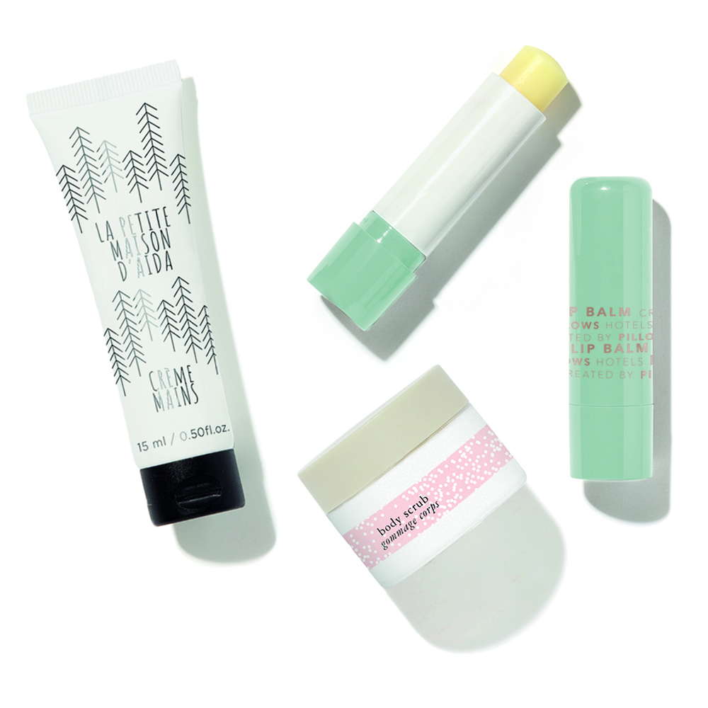 Eine flache Anordnung von vier Hautpflegeprodukten, darunter eine Handcremetube, ein Lippenbalsamstift, ein Tiegel Creme und ein weiterer Lippenbalsam, jeweils in verschiedenen Pastelltönen und Designs.