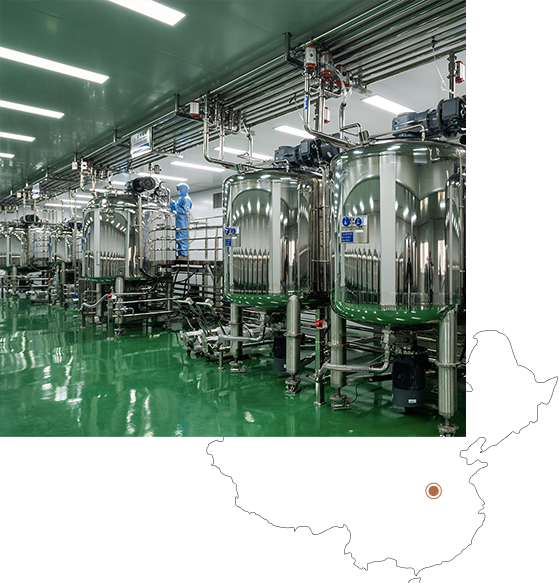 Uma instalação industrial limpa e moderna, com tanques e tubos de aço inoxidável, com um trabalhador em equipamento de proteção. O chão é brilhante e verde, indicando um ambiente higiénico.