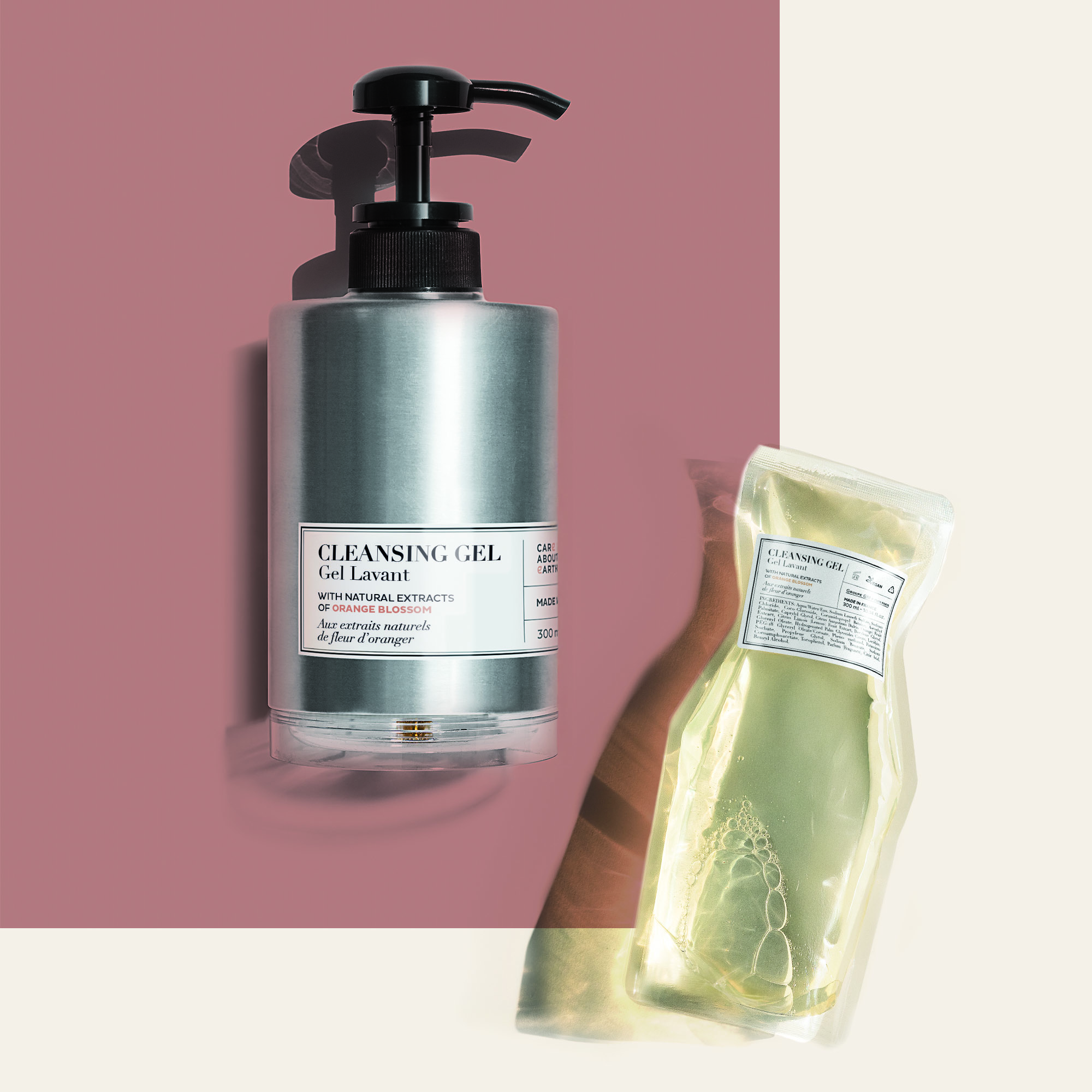 Eine elegante silberne Pumpflasche mit Reinigungsgel neben einer transparenten Verpackung mit einem grünen Gelprodukt vor einem zartrosa-cremefarbenen Hintergrund.