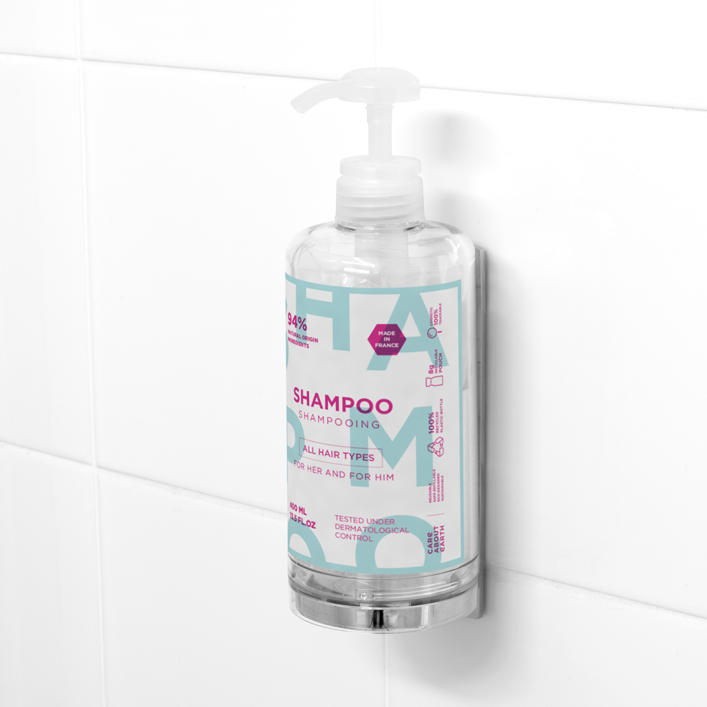 Μια διαφανής φιάλη σαμπουάν με την ένδειξη «Shampoo» και αντλία στο καπάκι, τοποθετημένη σε λευκό πλακάκι τοίχου, σχεδιασμένη για όλους τους τύπους μαλλιών. Η φιάλη έχει γαλάζια και ροζ χρώματα με διάφορα εικονίδια.