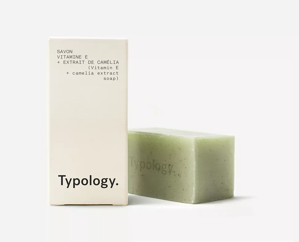 Ein Stück grüne Seife mit Vitamin E und Kamelienextrakt, neben der minimalistischen Verpackung mit dem Markennamen „Typology“.