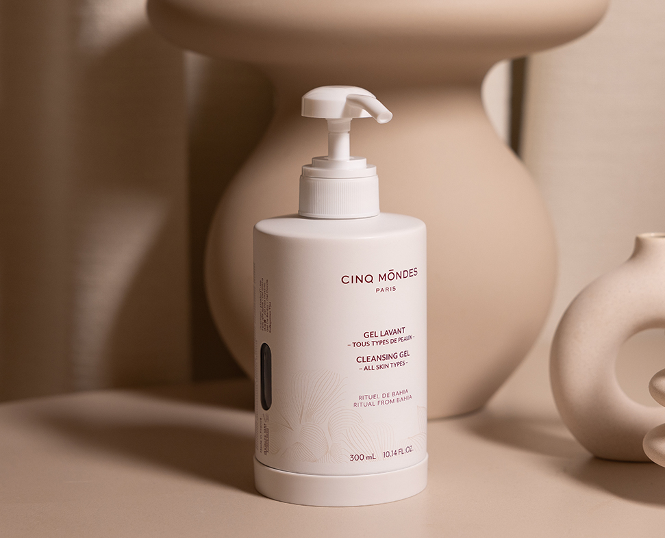 Um frasco de gel Cinq Mondes com dispensador, sobre um fundo neutro com formas suaves e orgânicas. O rótulo indica que é adequado para todos os tipos de pele.