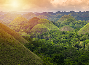 Un paesaggio pittoresco caratterizzato da dolci colline verdi sotto un tramonto dorato, circondato da una rigogliosa vegetazione tropicale.