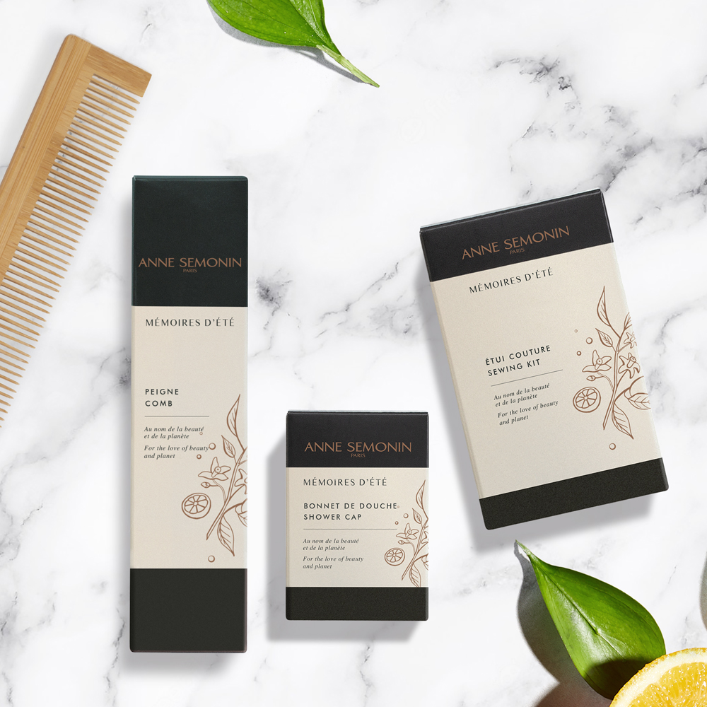 Uma composição plana com produtos de beleza Anne Semonin , incluindo um pente, touca de banho e um kit de costura, dispostos sobre um fundo de mármore com folhas decorativas.