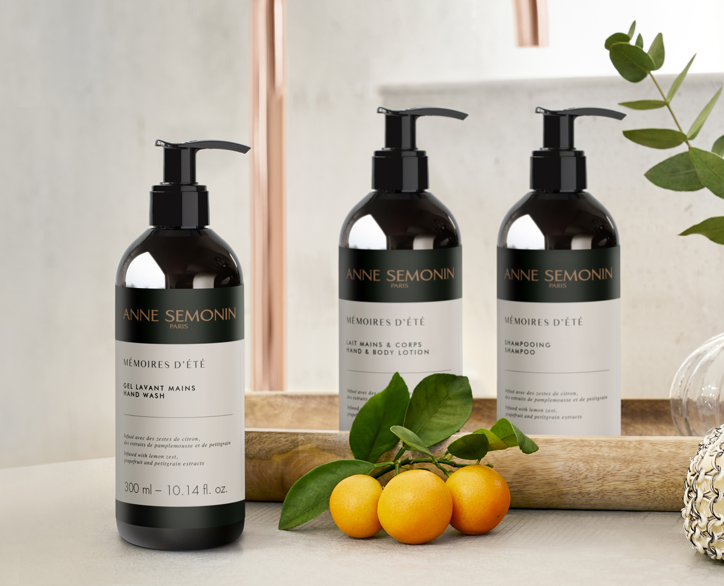 Três frascos pretos de produtos Anne Semonin e corpo Anne Semonin estão expostos sobre uma superfície de madeira, acompanhados por pequenos frutos alaranjados e folhas verdes. Os rótulos apresentam o texto «Mémoires d'Été» e descrevem a função de cada produto.