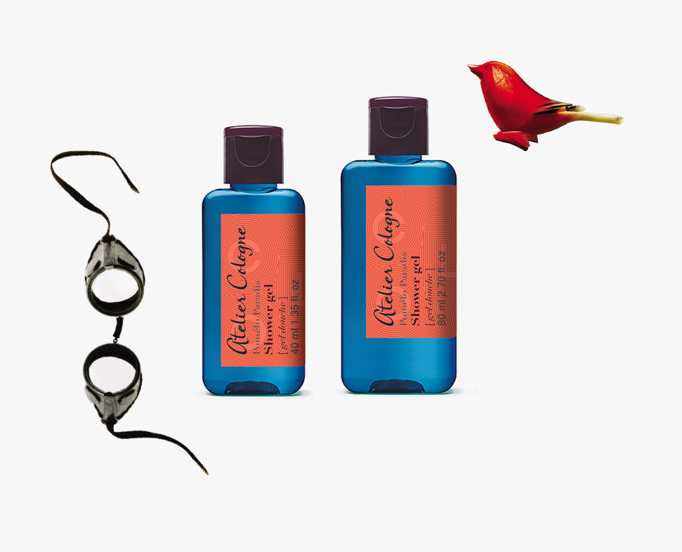 Zwei Flaschen Atelier Cologne Shampoo-Gel sind von einer Blume und einer schwarzen Schutzbrille umgeben.