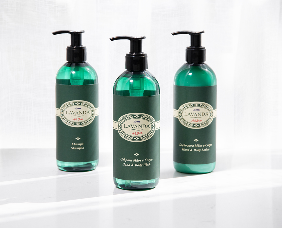 Tre flaconi di prodotti per la cura personale Lavanda - shampoo, detergente mani e corpo e lozione mani e corpo - con etichetta verde e dispenser a pompa, disposti su uno sfondo chiaro.