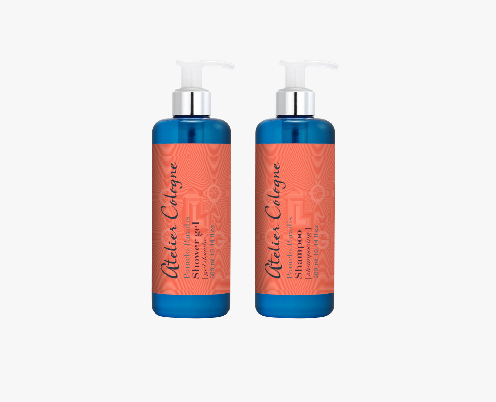 Zwei Flaschen Shampoo mit einem leuchtend blauen Design und korallenroten Etiketten mit der Aufschrift „Atelier Cologne“. Jede Flasche hat oben einen Pumpspender.