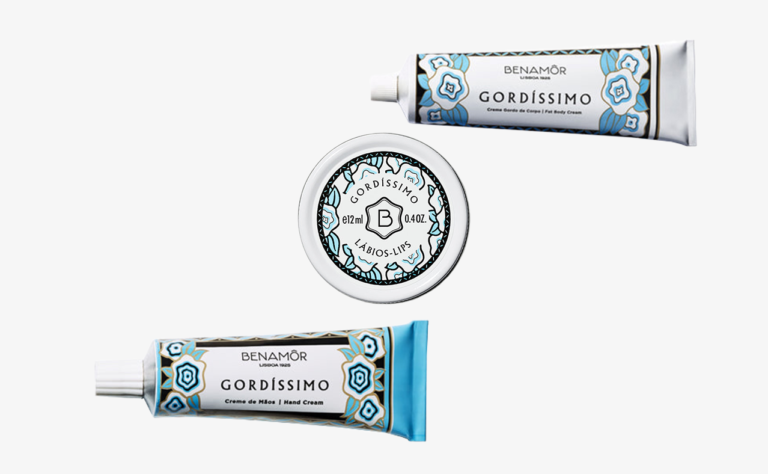 Una collezione di tubetti di crema per le labbra Benamor Gordíssimo e una scatola di latta, caratterizzati da intricati disegni blu e bianchi sulla confezione.