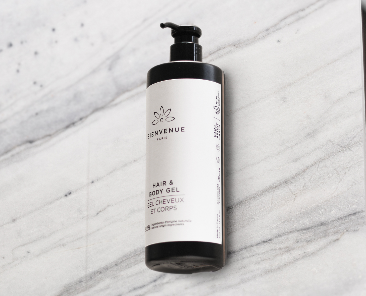 Eine Flasche Bienvenue Hair &amp; Body Gel steht auf einer Marmoroberfläche. Die Flasche hat eine schwarze Pumpe und ein minimalistisches weißes Etikett.