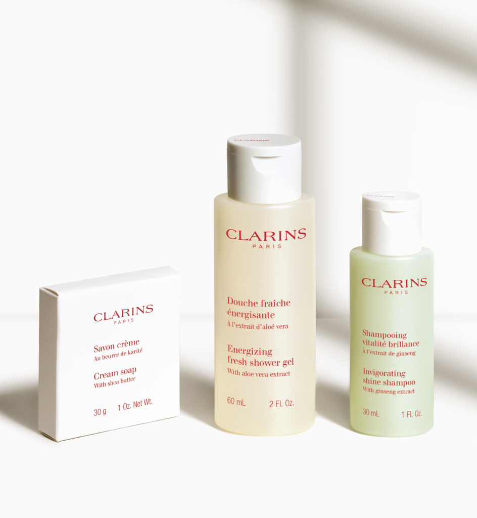 Eine Kollektion von Clarins , darunter eine cremige Seife, ein energiespendendes Duschgel und ein belebendes Glanzshampoo, präsentiert vor einem hellen Hintergrund.