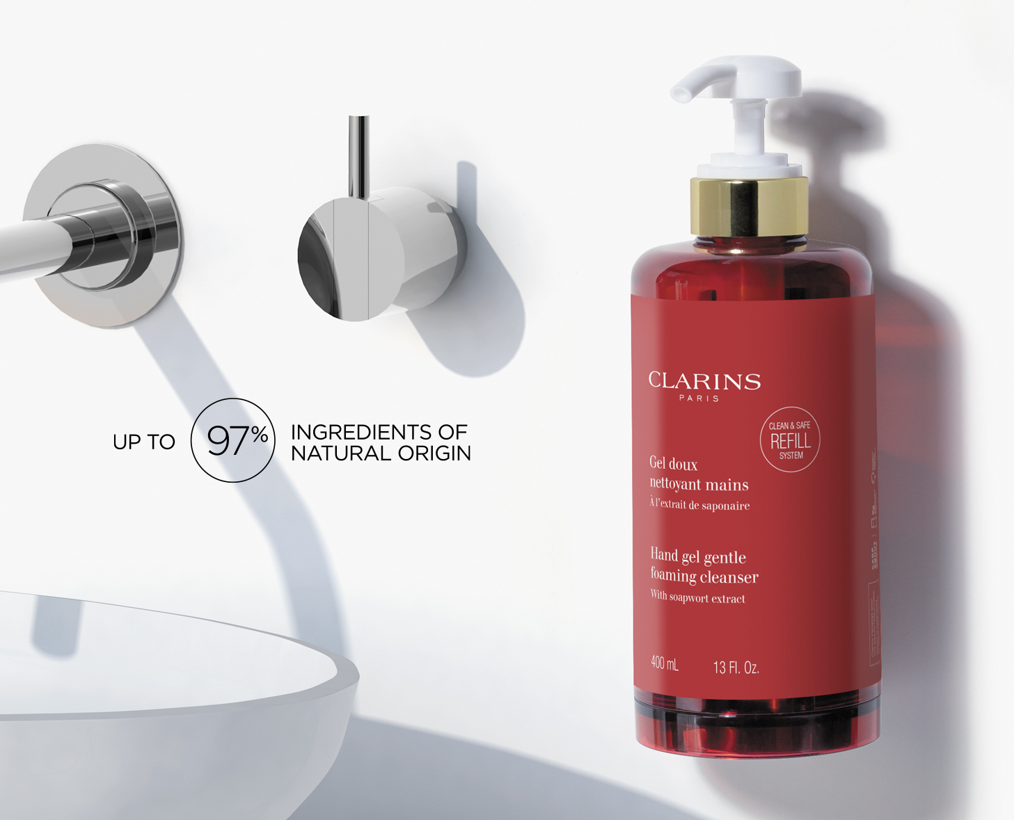 Eine rote Flasche Clarins Gentle Foaming Cleanser, die neben einem eleganten Wandwasserhahn ausgestellt ist. Das Etikett hebt hervor, dass „bis zu 97 % der Inhaltsstoffe natürlichen Ursprungs sind“.