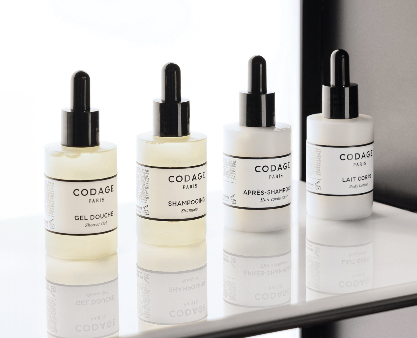 Vier Flaschen Hautpflegeprodukte von CODAGE in einer Reihe, mit Etiketten für Duschöl, Shampoo, Haarspülung und Körperlotion, alle in minimalistischem weißem Design.