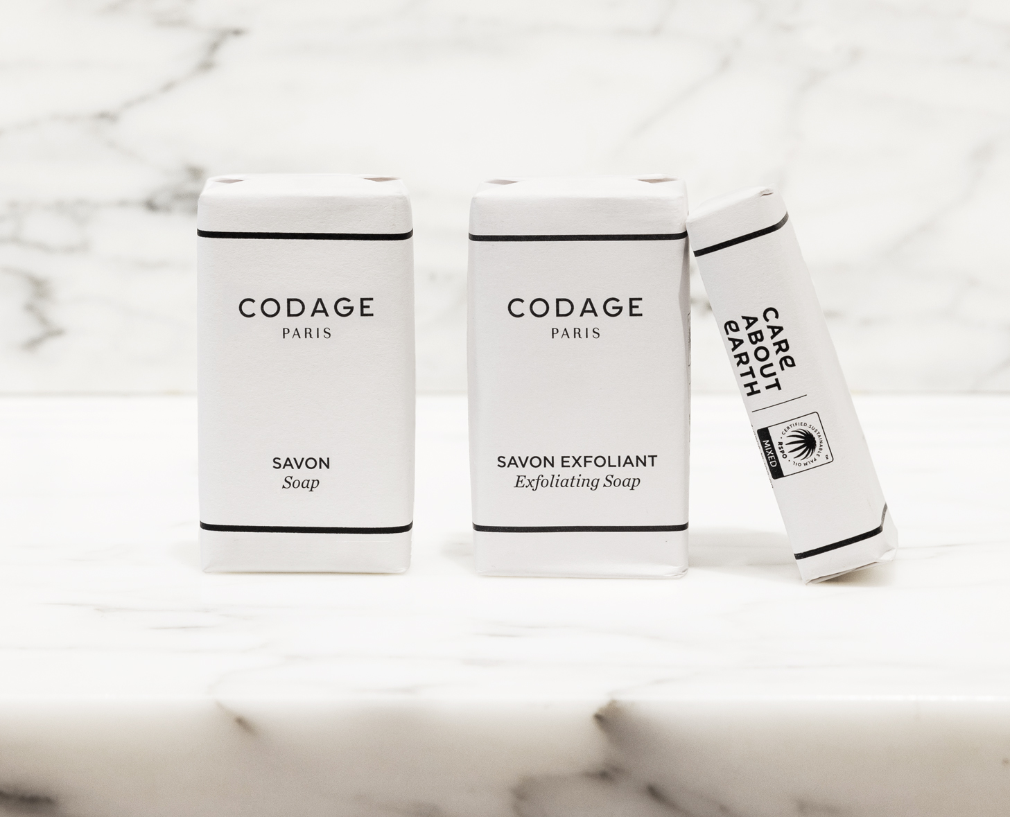 Zwei Seifenstücke in minimalistischer weißer Verpackung mit der Aufschrift „Savon” und „Savon Exfoliant” von Codage , präsentiert auf einer Marmoroberfläche.