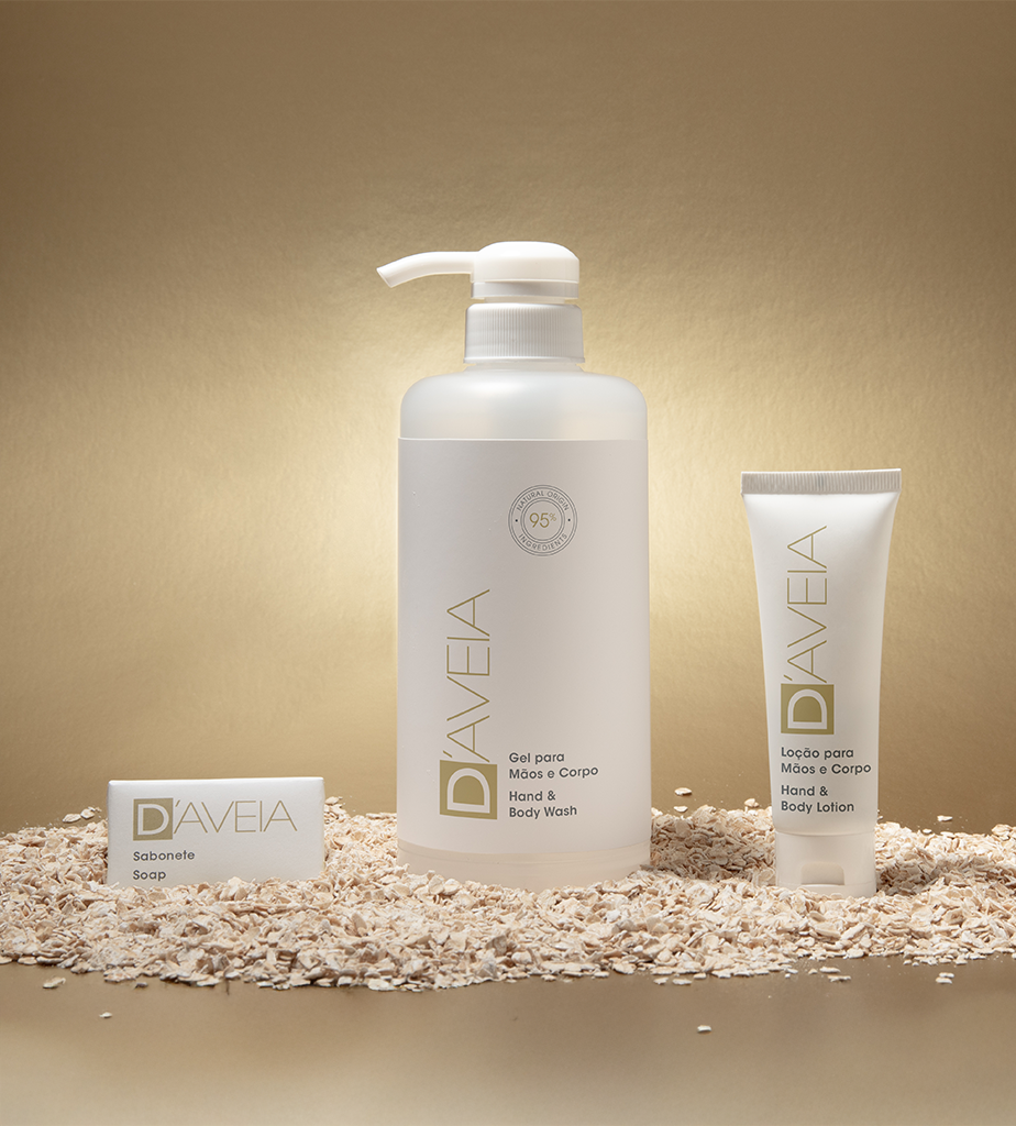 Um frasco de sabonete líquido para mãos e corpo e um tubo de loção para mãos e corpo repousam sobre um fundo de aveia, ao lado de uma barra de sabonete, todos com um design minimalista e uma paleta de cores neutras.