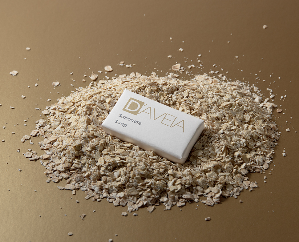 Uma barra de sabonete de aveia DAVEIA repousa sobre um monte de aveia num fundo dourado. O sabonete tem um design simples e elegante, com o nome da marca em destaque.