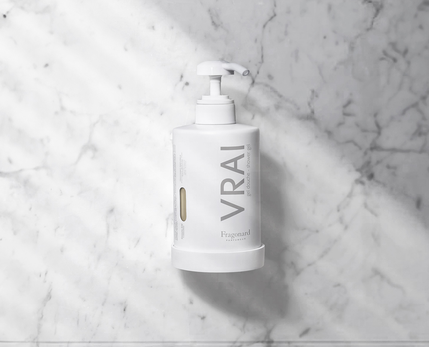 Una bottiglia bianca con pompa del detergente viso VRAI è esposta su uno sfondo di marmo chiaro. La bottiglia presenta un design minimalista con il nome del marchio ben visibile.