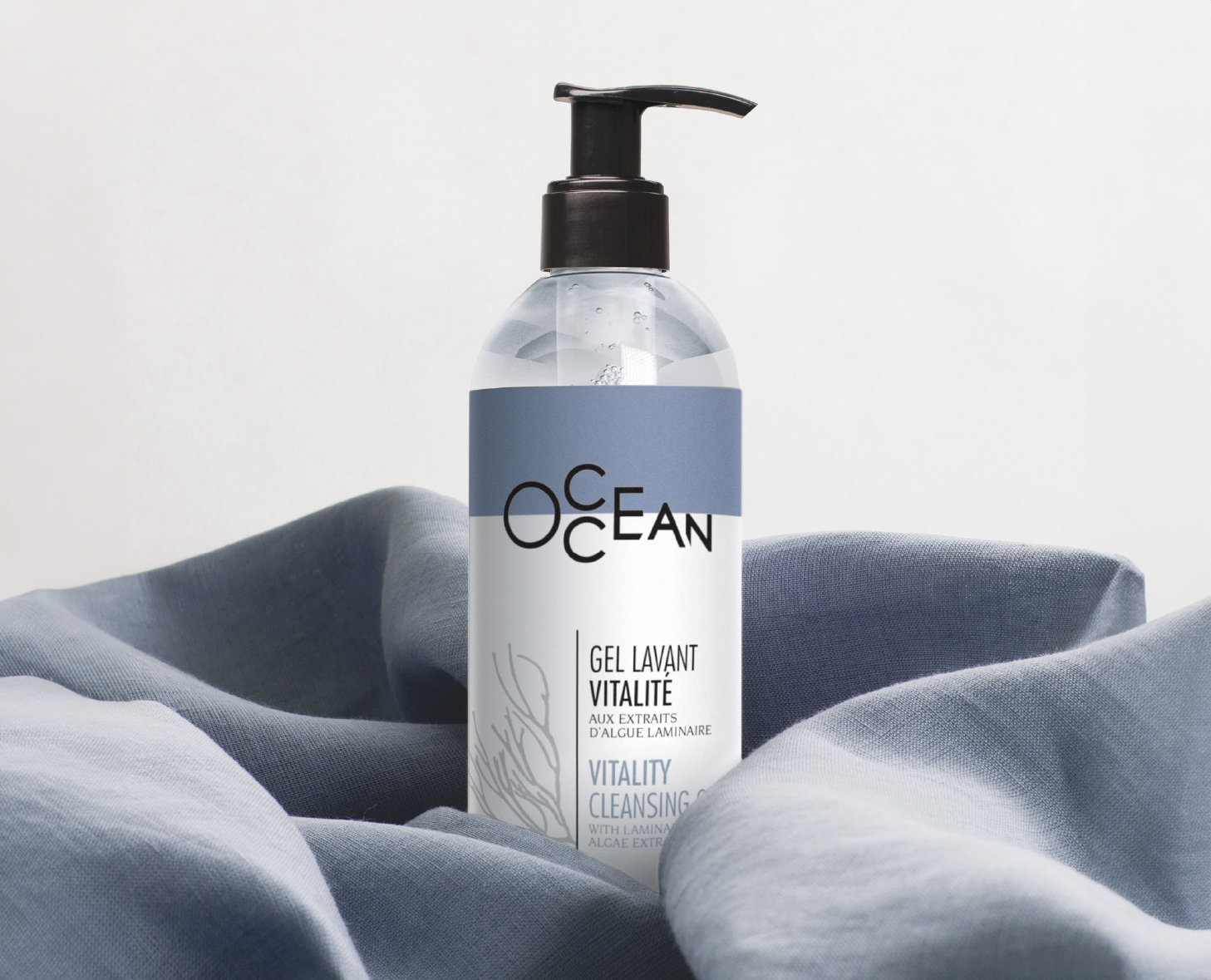 Una bottiglia trasparente di "OCEAN Vitality Cleansing Gel" con tappo a pompa, caratterizzata da un'etichetta moderna, posizionata su uno sfondo morbido in tessuto blu.
