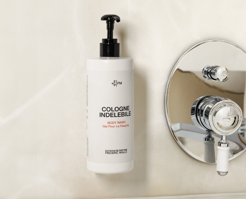 Eine weiße Flasche mit dem Aufdruck „Cologne Indelebile” ist neben einem runden Spiegel an der Wand befestigt. Die Flasche verfügt über einen schwarzen Pumpspender und ein minimalistisches Design.