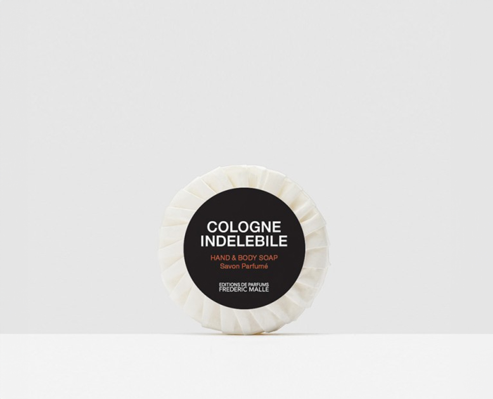Ein runder Seifenstück für Hände und Körper mit der Aufschrift „Cologne Indelebile” von Frédéric Malle, mit einem schwarz-weißen Design auf einfarbigem Hintergrund.