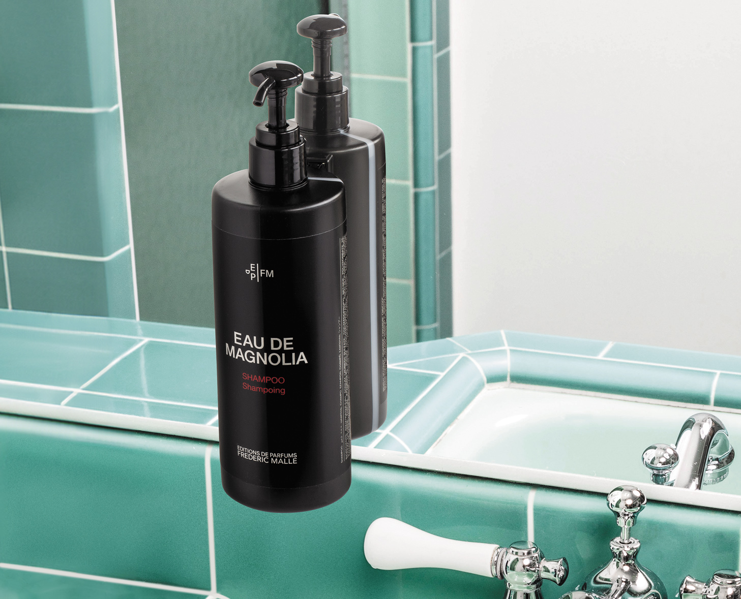 Un elegante flacone di shampoo nero con l'etichetta "Eau de Magnolia" è appoggiato accanto al lavandino e si riflette sulle piastrelle turchesi del bagno. L'ambiente moderno è caratterizzato da finiture eleganti e un design raffinato.