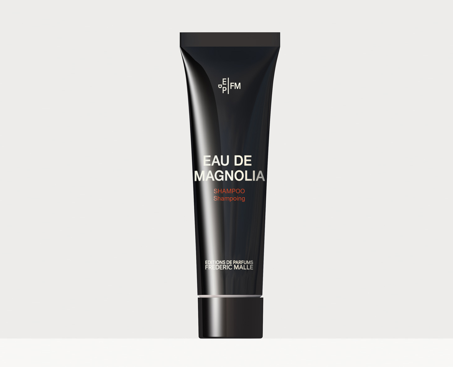 Un elegante tubetto di shampoo nero con l'etichetta "Eau de Magnolia" di Éditions de Parfums Frédéric Malle. Il design è moderno e minimalista.