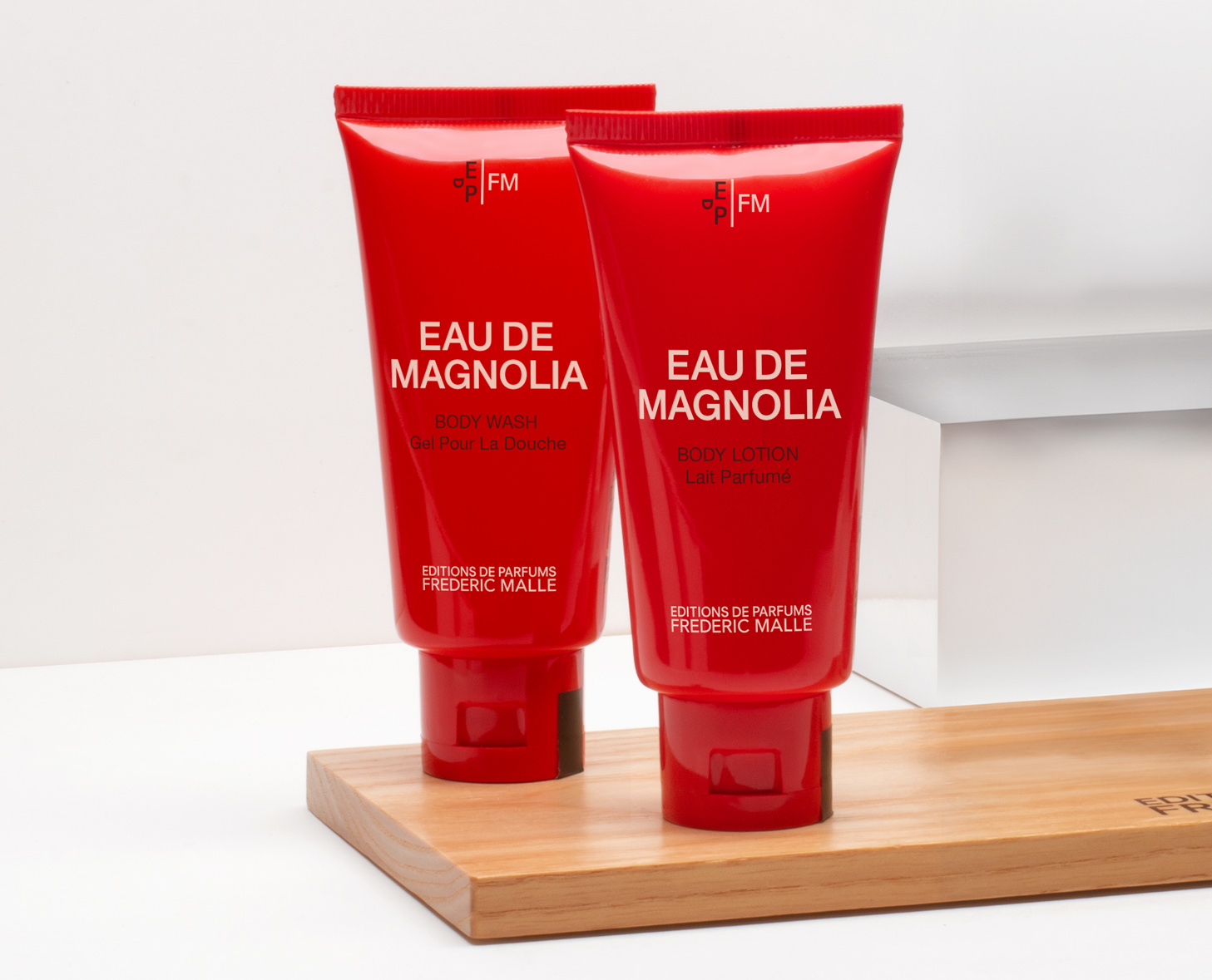 Due tubetti rossi di bagnoschiuma e lozione per il corpo con l'etichetta "Eau de Magnolia" appoggiati su una superficie di legno.