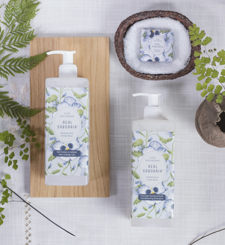 Una composizione piatta di prodotti per la cura della pelle con due flaconi etichettati "Real Saboría" su una superficie bianca ruvida, accompagnati da una piccola ciotola decorativa con sale e foglie verdi. I flaconi sono decorati con motivi floreali.