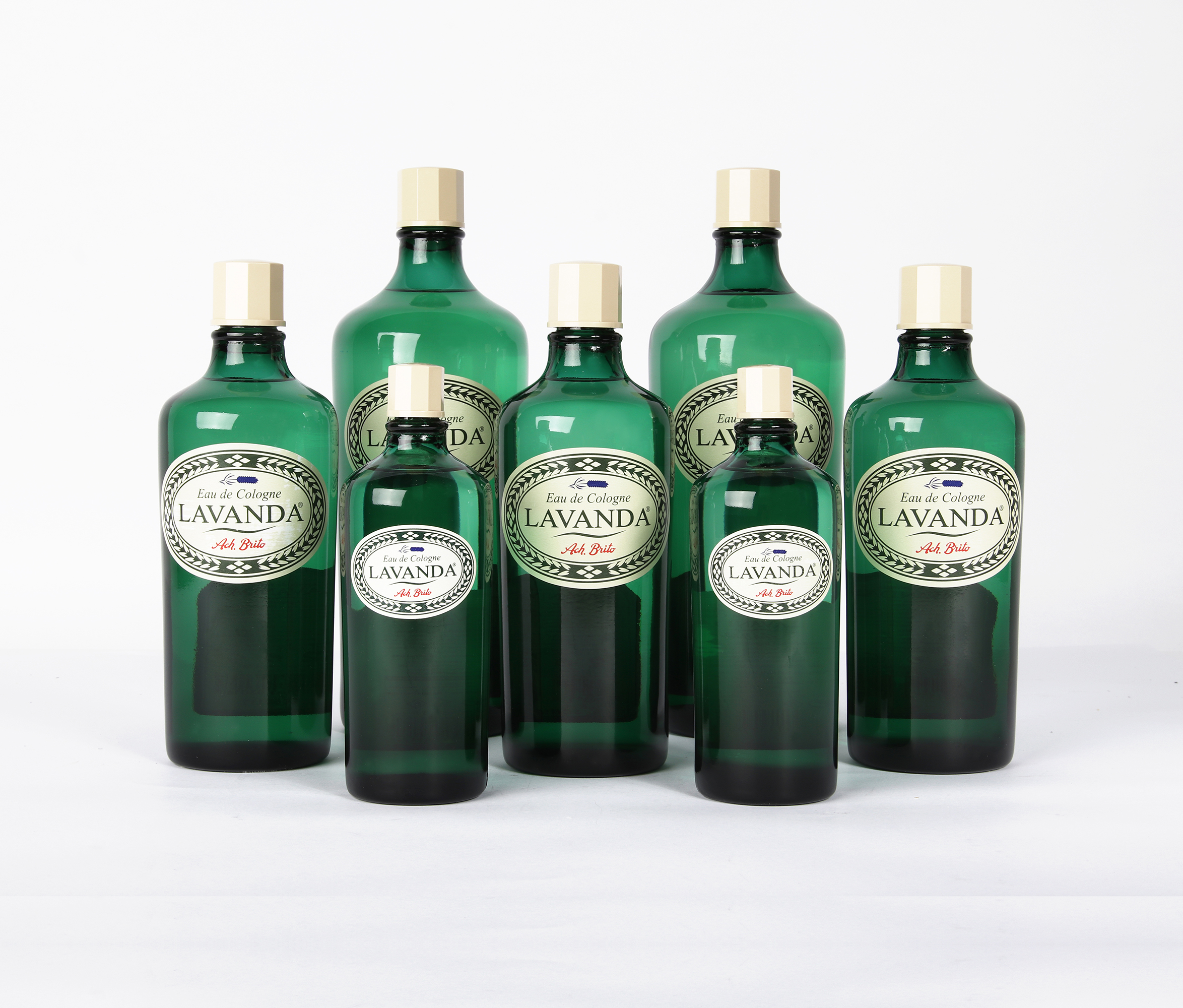 Un gruppo di otto bottiglie di vetro verde di varie dimensioni, tutte etichettate "Lavanda", disposte ad arte su uno sfondo bianco. Ogni bottiglia è dotata di un tappo dorato e di un'etichetta decorativa.
