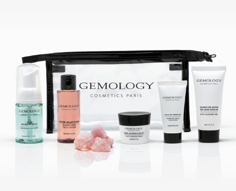 Eine durchsichtige Kosmetiktasche mit verschiedenen Gemology , darunter eine Feuchtigkeitscreme, ein Gesichtswasser und eine Gesichtsmaske, sowie rosa Mineralkristalle.