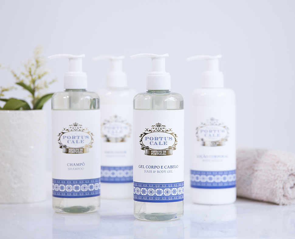 Una collezione di quattro flaconi di prodotti per la cura personale, tra cui shampoo e gel per capelli e corpo, esposti su una superficie di marmo accanto a una piccola pianta in vaso.