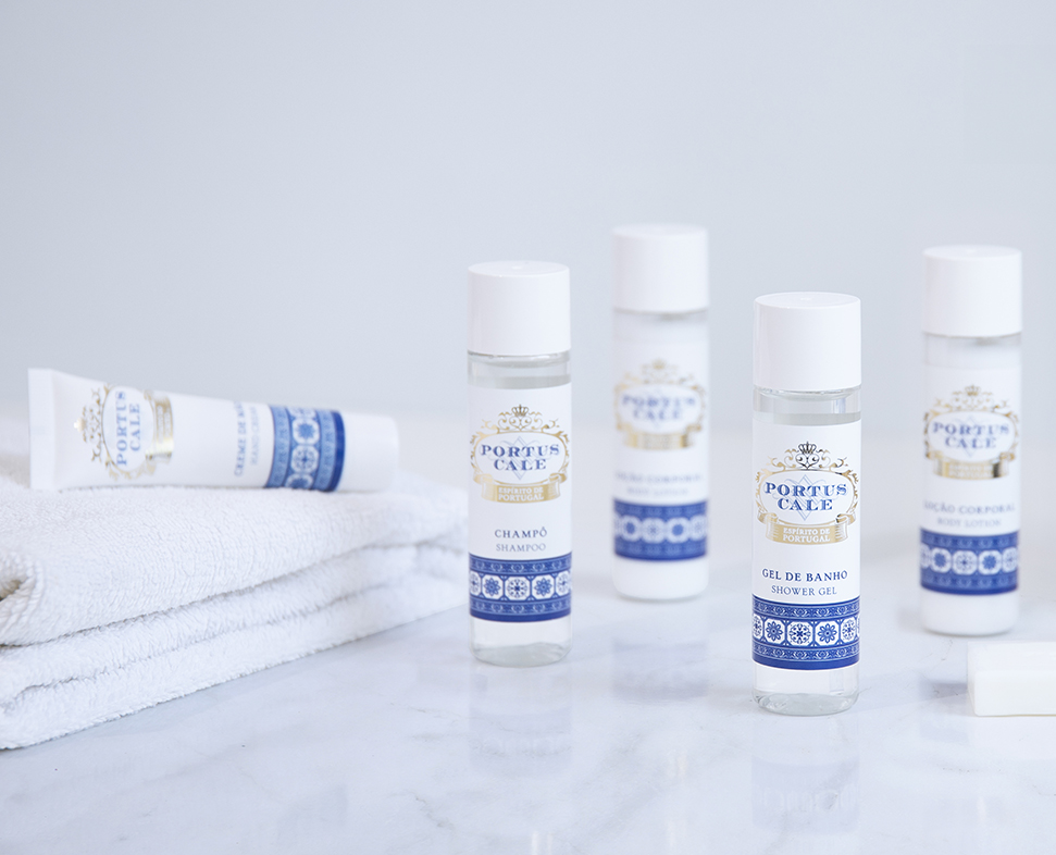 Una collezione ordinatamente disposta di articoli da bagno Portus Cale, tra cui shampoo, bagnoschiuma e gel condizionante, accanto a un asciugamano bianco su una superficie di marmo.